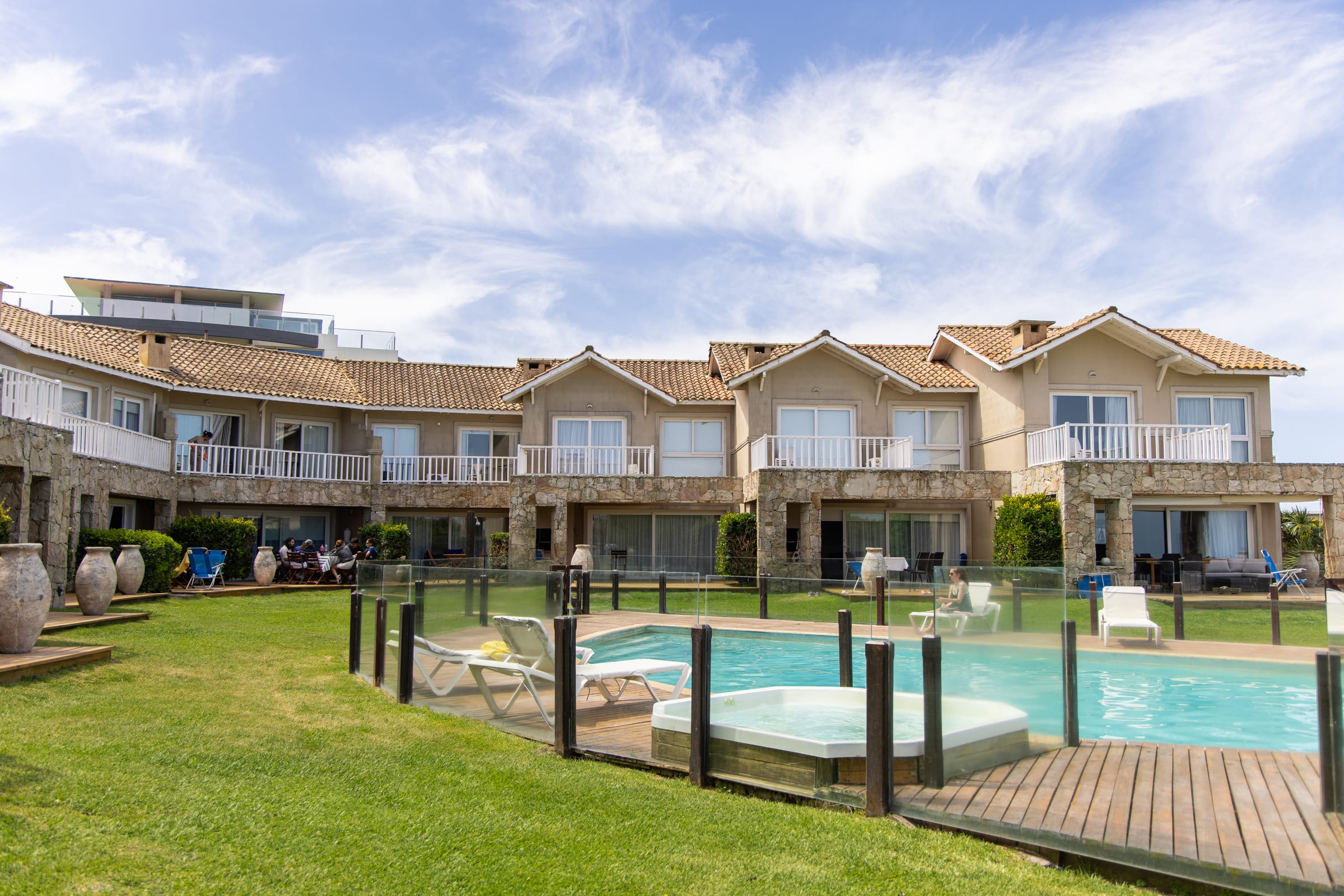 La pileta con deck de madera y reposeras, las casas detrás y el jacuzzi en primer plano.